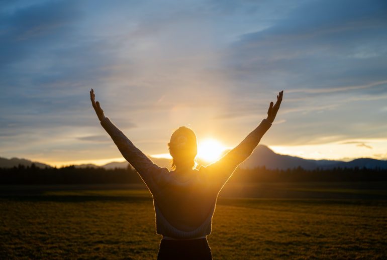 Woman embracing life standing outside in beautiful meadow with her arms raised high
